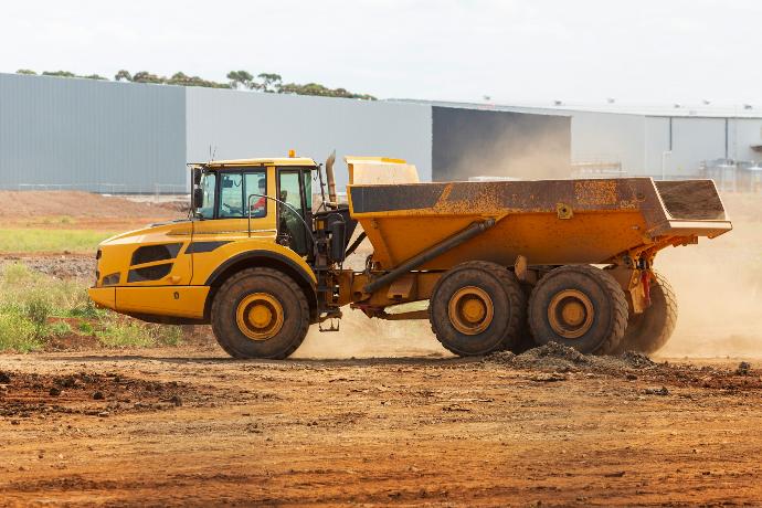 a yellow dump truck driving down a dirt road